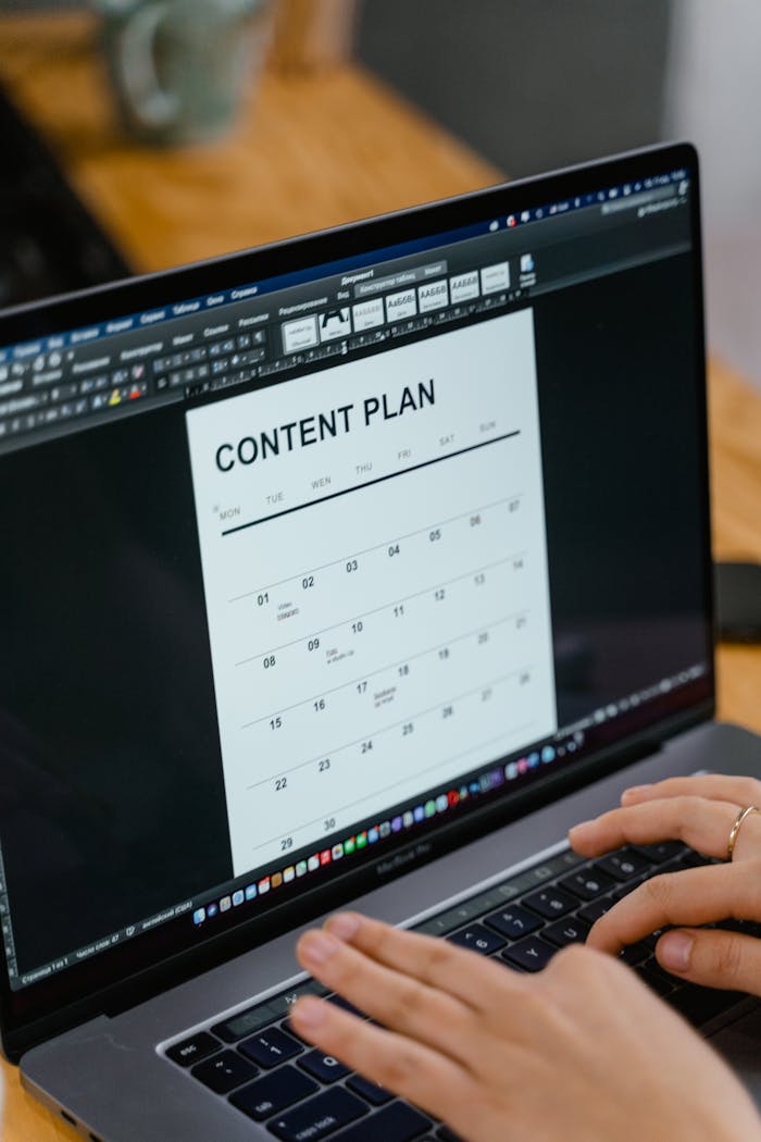 gallery-04 Close-up of hands typing on a laptop displaying a content plan document, ideal for business or marketing content.